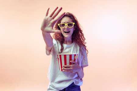 Portrait of young girl in casual outfit posing with popcorn basket isolated over pink studio...