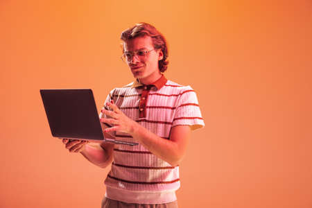 Portrait of young man in glasses with laptop, working, posing isolated over orange studio background...