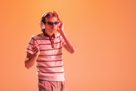Portrait of young man in trendy sunglasses listening to music in headphones, enjoying isolated over...