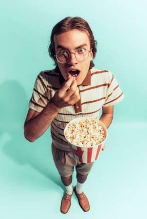 Portrait of young emotive man posing with popcorn basket isolated over light blue studio background. Watching interesting movies. Concept of youth, fashion, lifestyle, emotions. Copy space for adの写真素材