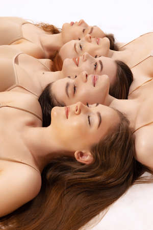 Close-up portrait of beautiful women lying on floor head to head in mosaic style isolated over white studio background. Concept of natural beauty, body and skin care, health, spa, cosmetics, adの写真素材