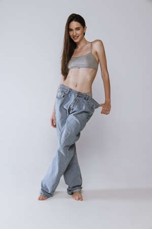 Portrait of beautiful young woman posing in big jeans and cotton top isolated over grey studio background. Smilng. Concept of beauty, body and skin care, health, spa, sport, cosmetics, adの写真素材