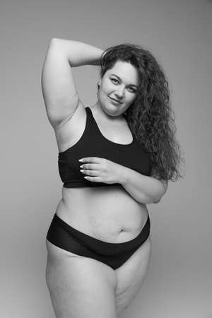 Portrait of young beautiful woman with curly hair posing in black underwear. Black and white photography. Self-acceptance. Concept of beauty, body and skin care, health, plastic surgery, cosmetics, adの写真素材