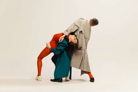 Portrait of stylish man and woman in coats and tights posing isolated over grey studio background....