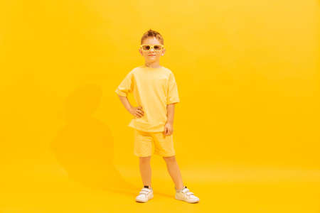 Portrait of cheerful little boy, child in bright summer outfit and sunglasses posing isolated over...