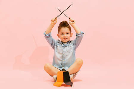 Portrait of little boy, child in jeans t-shirt playing fake drums, having fun, posing isolated over pink background. Cheerful musician. Concept of childhood, family, emotions, lifestyle, fashion, adの写真素材