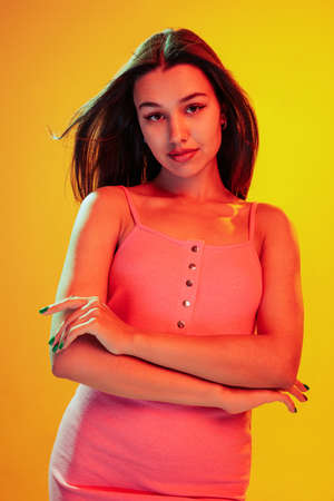 Portrait of beautiful young girl posing, attentively looking at camera isolated over yellow...