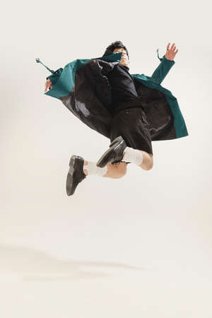 Portrait of stylish young man in black outfit and green coat posing isolated over grey studio background. Jumping . Concept of modern fashion, art photography, style, queer, uniqueness, adの写真素材