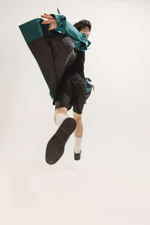 Portrait of stylish young man in black outfit and green coat posing isolated over grey studio...