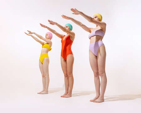 Three young women in vintage retro swimming suits posing isolated over grey studio background. Sportive lifestyle. Concept of beauty, fashion, vintage style, summertime, party. Copy space for adの写真素材