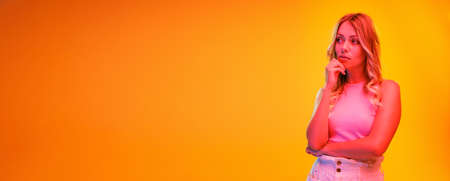 Portrait of young beautiful woman posing isolated over yellow background in neon light. Thoughtful look. Concept of beauty, emotions, facial expression, lifestyle, fashion, youth culture. Flyerの写真素材