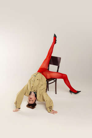 Portrait of young girl in red tights and stylish jacket posing, falling down the chair isolated over...