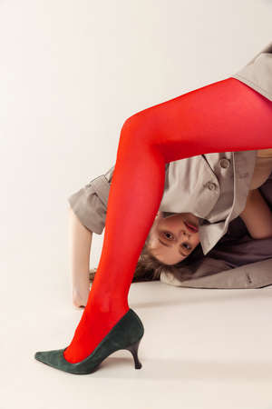 Portrait of young woman in red tights and heels standing on head, posing isolated over grey studio background . Concept of retro fashion, art photography, style, queer, beautyの写真素材