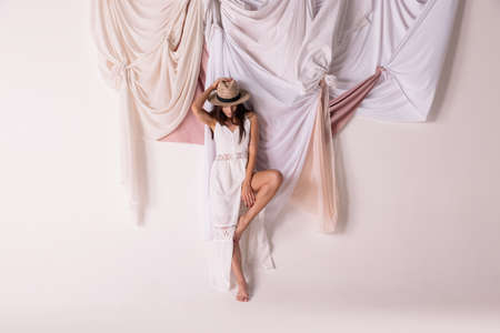 Portrait of beautiful woman in white dress and straw hat posing isolated grey background with textile design. Concept of natural beauty, fashion, wellness, lifestyle, femininity, summer style, adの写真素材