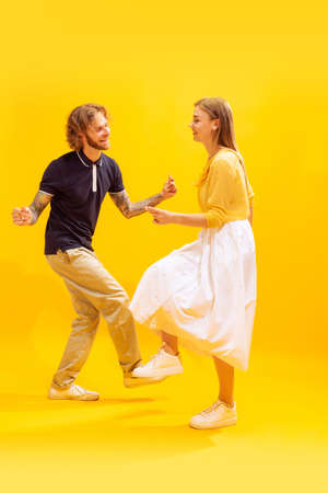 Portrait of young man and woman dancing, posing isolated over yellow studio background. Retro dance moves. Concept of youth, lifestyle, relationship, emotions, facial expression, adの写真素材