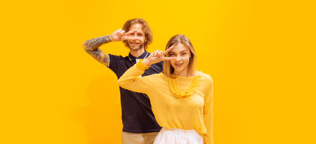 Portrait of young man and woman in casual clothes posing isolated over yellow studio background....