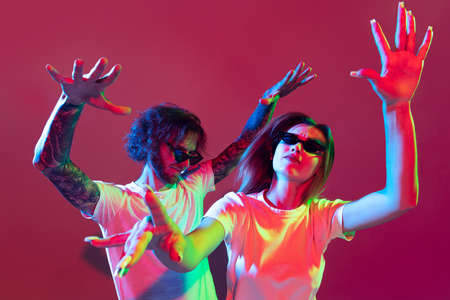 Portrait of young stylish man and woman dancing, posing isolated over red background in neon light....