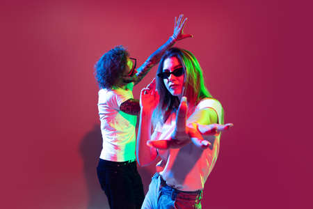 Portrait of young stylish man and woman dancing, posing isolated over red background in neon light....