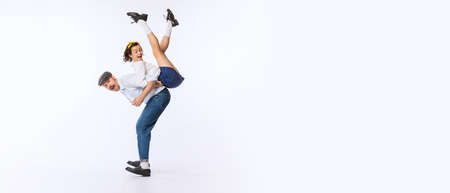 Portrait of young cheerful couple, man and woman, in stylish retro outfit dancing isolated on white...