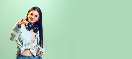 Portrait of young girl, student in casual clothes posing isolated over green studio background. New...
