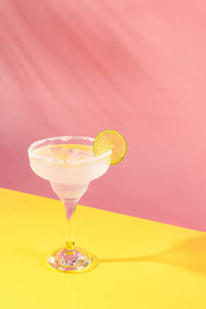 Glass of delicious margarita cocktail isolated over pink yellow background. Popular taste. Party time. Concept of cocktails, alcoholic drinks, taste, party, mix. Copy space for ad. Retro styleの写真素材