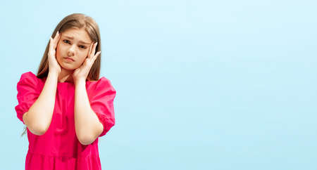 Portrait of beautiful, emotive young girl posing isolated over blue studio background. Sad, tired...