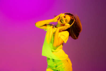 Portrait of young girl listening to music in headphones isolated over pink background in neon light. Concept of beauty, style, lifestyle, youth, emotions, facial expression. Copy space for adの写真素材