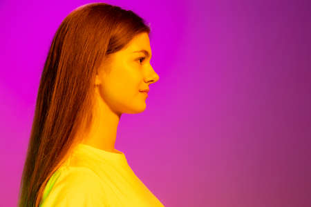 Portrait of young girl posing, calmly looking isolated over pink background in neon light. Concept...
