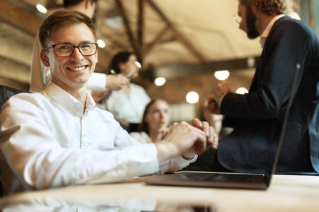 Young smiling man in official clothes and glasses, working on laptop at stylish modern office....