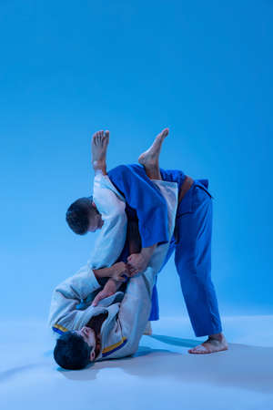 Portrait of judo athletes training, practising throws isolated over blue background in neon light....