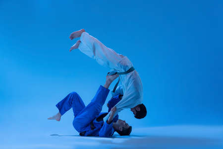 Dynamic portrait of professional judo coach training with athlete isolated over blue background in neon light. Concept of martial art, combat sport, health, strength, energy, fit. Copy space for adの写真素材