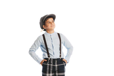Portrait of stylish kid, boy in shirt, cap, suspenders and plaid pants smiling, posing isolated over white studio background. Concept of childhood, friendship, fun, lifestyle, fashion. Retro styleの写真素材