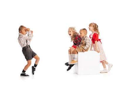 Portrait of little stylish children, boy taking photo with retro camera of laughing kids isolated over white studio background. Concept of childhood, friendship, fun, lifestyle, fashion. Retro styleの写真素材