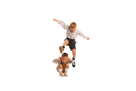 Portrait of two boys, children in retro clothes playing together, jumping isolated over white studio background. Concept of childhood, friendship, fun, lifestyle, fashion. Retro styleの写真素材
