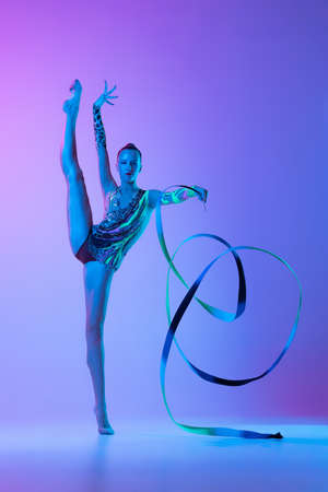 Portrait of tender young girl standing on twine with ribbons, posing isolated on pink purple background in neon light. Concept of action, motion, sport life, motivation, competition. Copyspace for adの写真素材