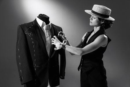 Portrait of beautiful woman in image of famous fashion designer working on male classic suit. Black and white photography. Simplicity. Monochrome effect. Concept of fashion, style, historyの写真素材