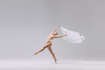 Portrait of young tender ballerina dancing with fabric isolated over grey studio background. Theatrical performance. Concept of classic ballet, inspiration, beauty, dance, creativityの写真素材