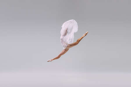 Portrait of young ballerina dancing, jumping in a twine with transparent fabric isolated over grey studio background. Concept of classic ballet, inspiration, beauty, dance, creativityの写真素材