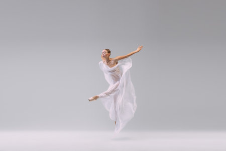 Portrait of young artistic ballerina dancing with transparent fabric isolated over grey studio background. Flexibility. Concept of classic ballet, inspiration, beauty, dance, creativityの写真素材