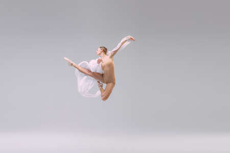 Portrait of young ballerina dancing with fabric isolated over grey studio background. Looks weightless, flexible. Fashion, style. Concept of classic ballet, inspiration, beauty, dance, creativityの写真素材