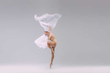 Portrait of young graceful ballerina dancing with fabric isolated over grey studio background. Classical tender movements. Concept of classic ballet, inspiration, beauty, dance, creativityの写真素材
