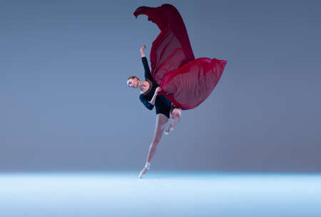 Portrait of young ballerina dancing with fabric isolated over blue grey studio background. Graceful tender performer of classic dance. Concept of classic ballet, inspiration, beauty, dance, creativityの写真素材