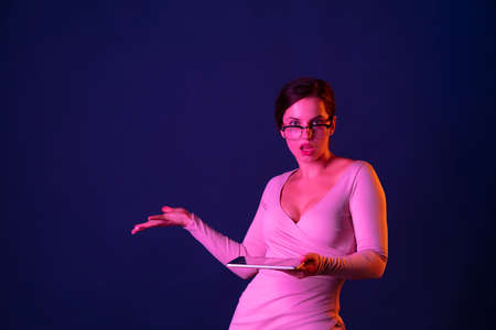 Portrait of young beautiful woman posing in stylish dress with tablet isolated over blue background...