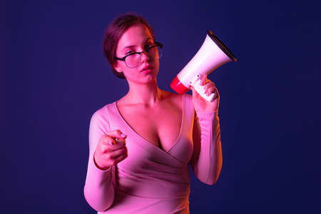 Portrait of young beautiful woman holding megaphone, pointing at camera isolated over purple...