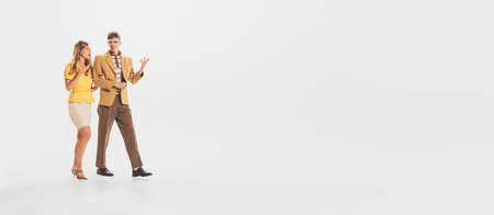Portrait of young couple, man and woman lively talking discussing while walking isolated over white studio background. Concept of retro fashion, style, youth culture, emotions, relationship, adの写真素材