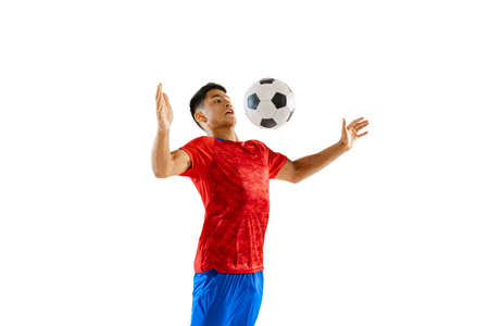 Dynamic portrait of young man, football player in motion, training, kicking ball with chest isolated on white studio background. Concept of sport, team game, action, motion. Copy space for ad, posterの写真素材