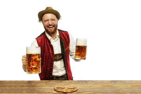 Portrait of young cheerful man wearing traditional Bavarian or German clothes holding big mugs with foamy beer isolated over white background. Alcohol, festival, traditions, holidays, taste concept.の写真素材