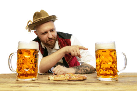 Portrait of young man wearing traditional Bavarian or German clothes isolated over white background. Giant mugs with foamy lager beer. Alcohol, Oktoberfest festival, traditions, taste concept.の写真素材