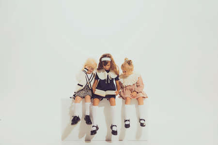 Three girls, children in vintage clothes sitting together, reading, doing homework isolated over...