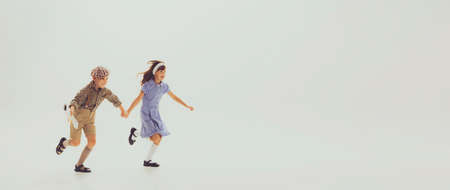 Portrait of stylish children, boy and girl, holding hands, running, posing isolated over grey studio background. Concept of childhood, friendship, fun, lifestyle, fashion, retro styleの写真素材